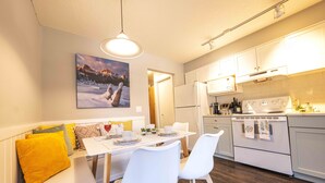 A modern kitchen with white cabinets, a dining table with chairs, and a painting of a snowy landscape on the wall.
