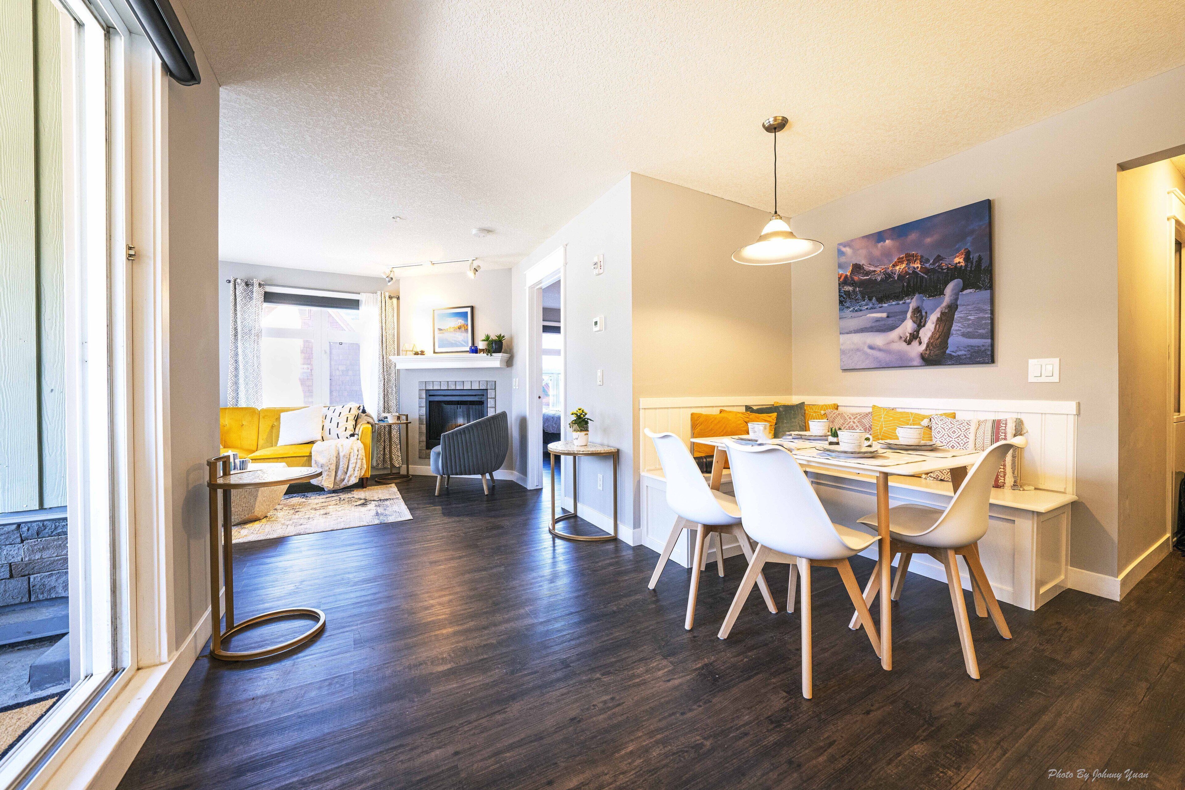 Une cuisine moderne avec un coin repas, un plancher en bois foncé et une grande fenêtre.