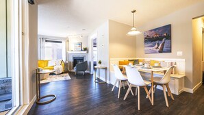 A modern kitchen with a dining area, dark wooden flooring, and a large window.