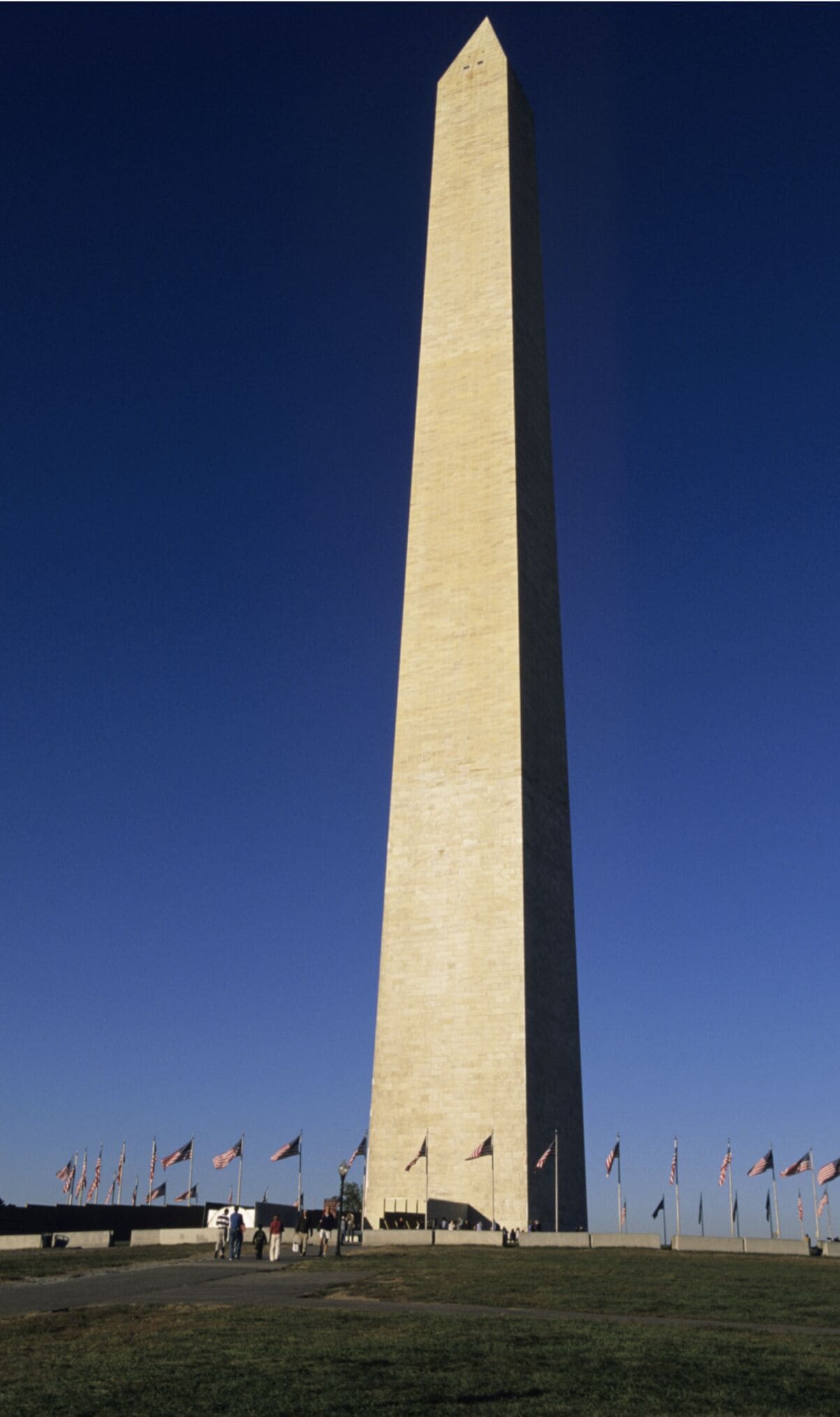 A tall, narrow obelisk with a flat top, surrounded by a grassy area and multiple American flags.