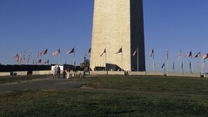 A tall, narrow obelisk with a flat top, surrounded by a grassy area and multiple American flags.