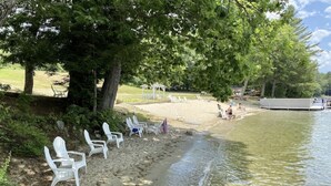 Ein Strand mit weißen Liegestühlen, einem Pavillon und einem Boot, das am Wasser liegt.