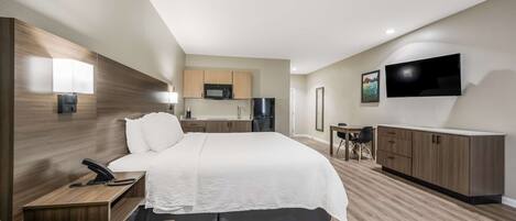 A modern hotel room with a large bed, a desk with a telephone, a small table with a chair, a microwave, a refrigerator, and a TV mounted on the wall.