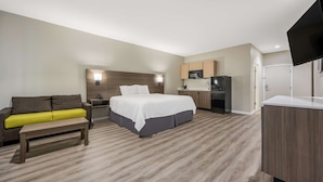 A modern hotel room with a bed, a sofa, a bench, a kitchenette, and a flat-screen TV. - SureStay Studio by Best Western Conroe Downtown (Conroe)