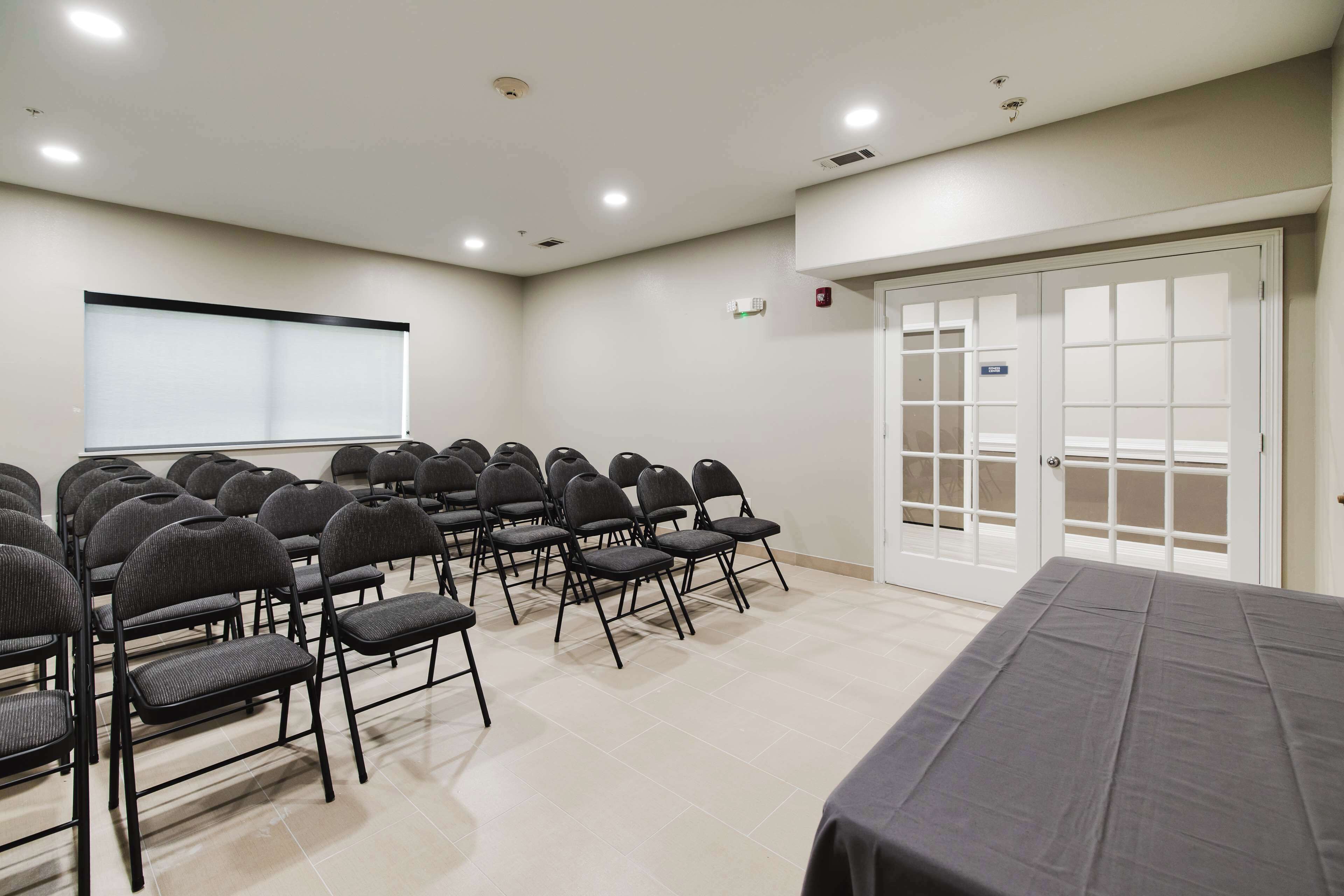 A conference room with rows of chairs, a projection screen, and a large table.