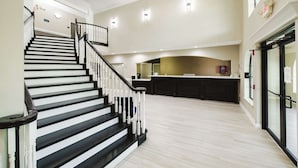 A spacious interior with a staircase leading to an upper level, a kitchen area, and a glass door entrance. - SureStay Studio by Best Western Conroe Downtown (Conroe)