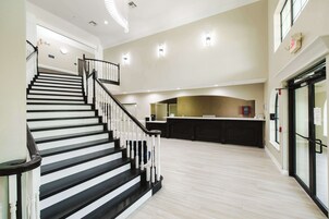 Un interior amplio con una escalera que conduce a un nivel superior, una zona de cocina y un acceso con puerta de cristal.