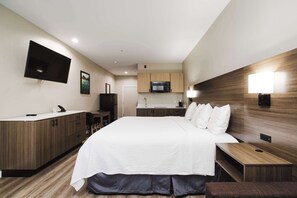 A modern hotel room with a large bed, a desk, a flat-screen TV mounted on the wall, a microwave, and a small kitchenette.