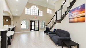 A spacious lobby with a staircase, a reception desk, and a large window with a view of the sunset. - SureStay Studio by Best Western Conroe Downtown (Conroe)