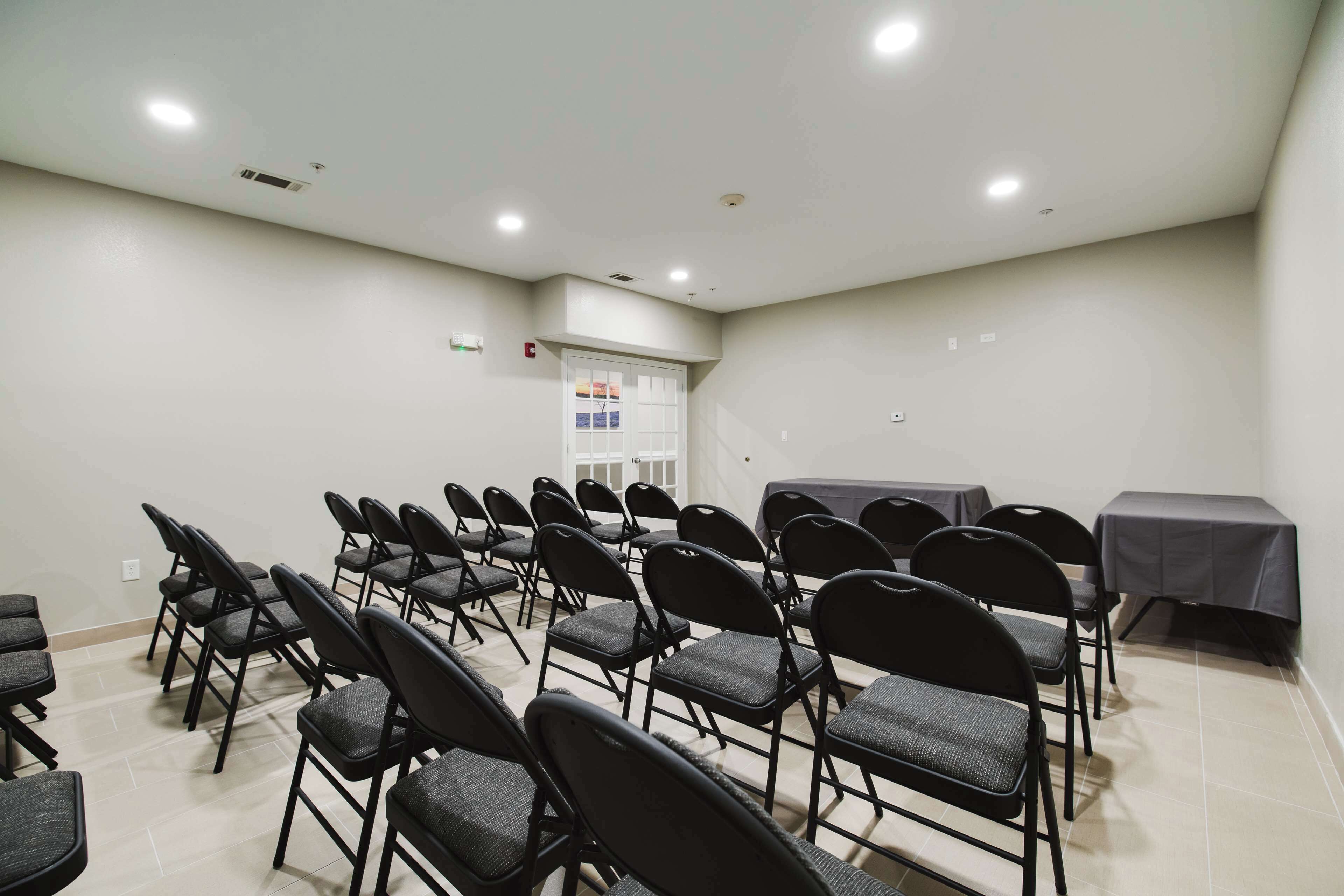 A conference room with rows of chairs, a table, and a door with a window.