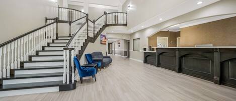 A spacious lobby with a staircase, seating area, and reception desk.