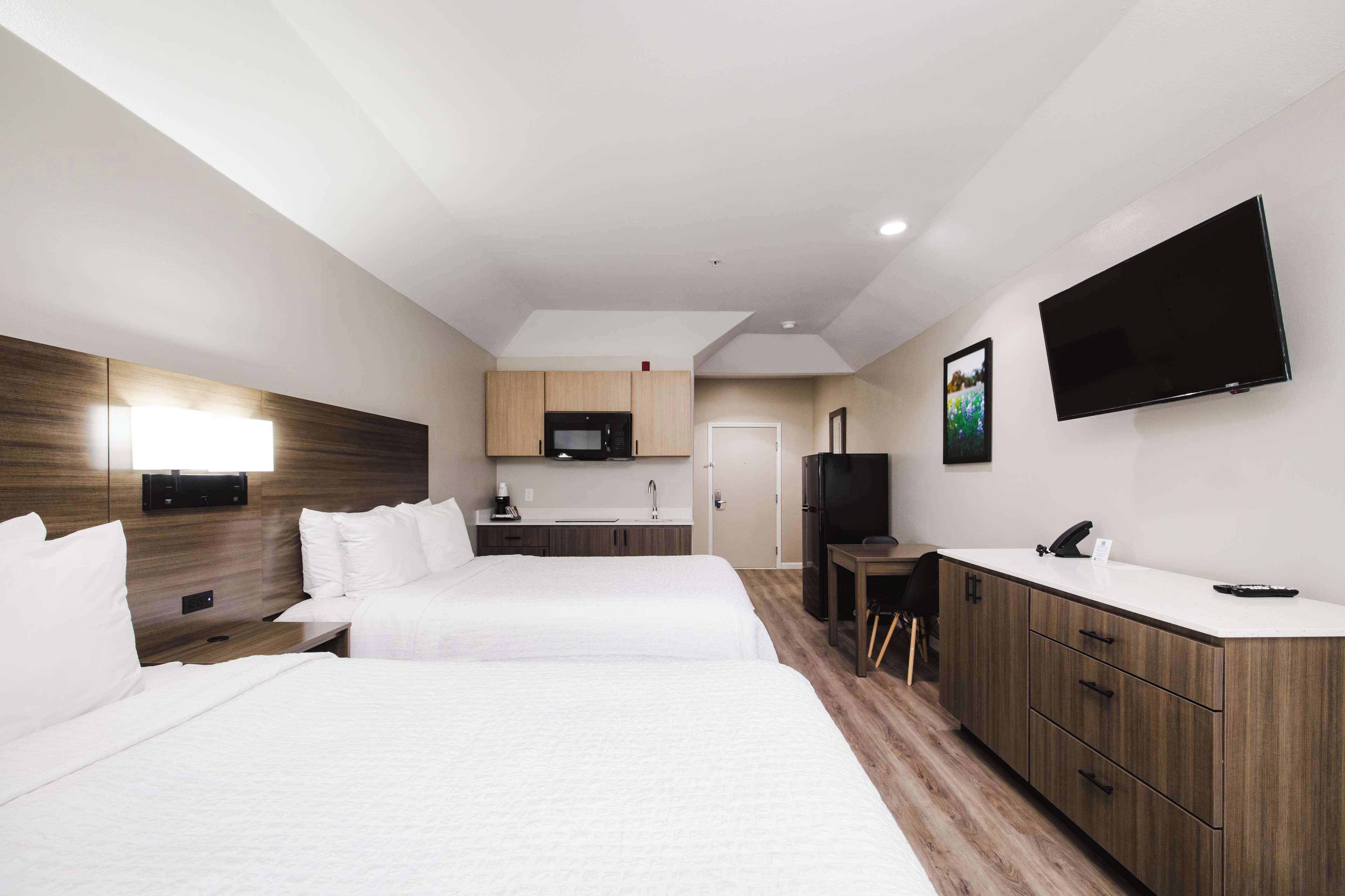 A hotel room with two beds, a kitchenette, a TV, and a desk.