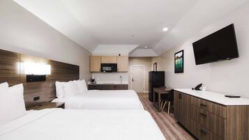 A hotel room with two beds, a kitchenette, a TV, and a desk.