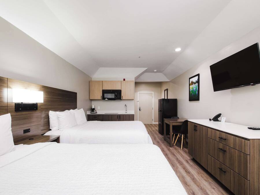 A hotel room with two beds, a kitchenette, a TV, and a desk.