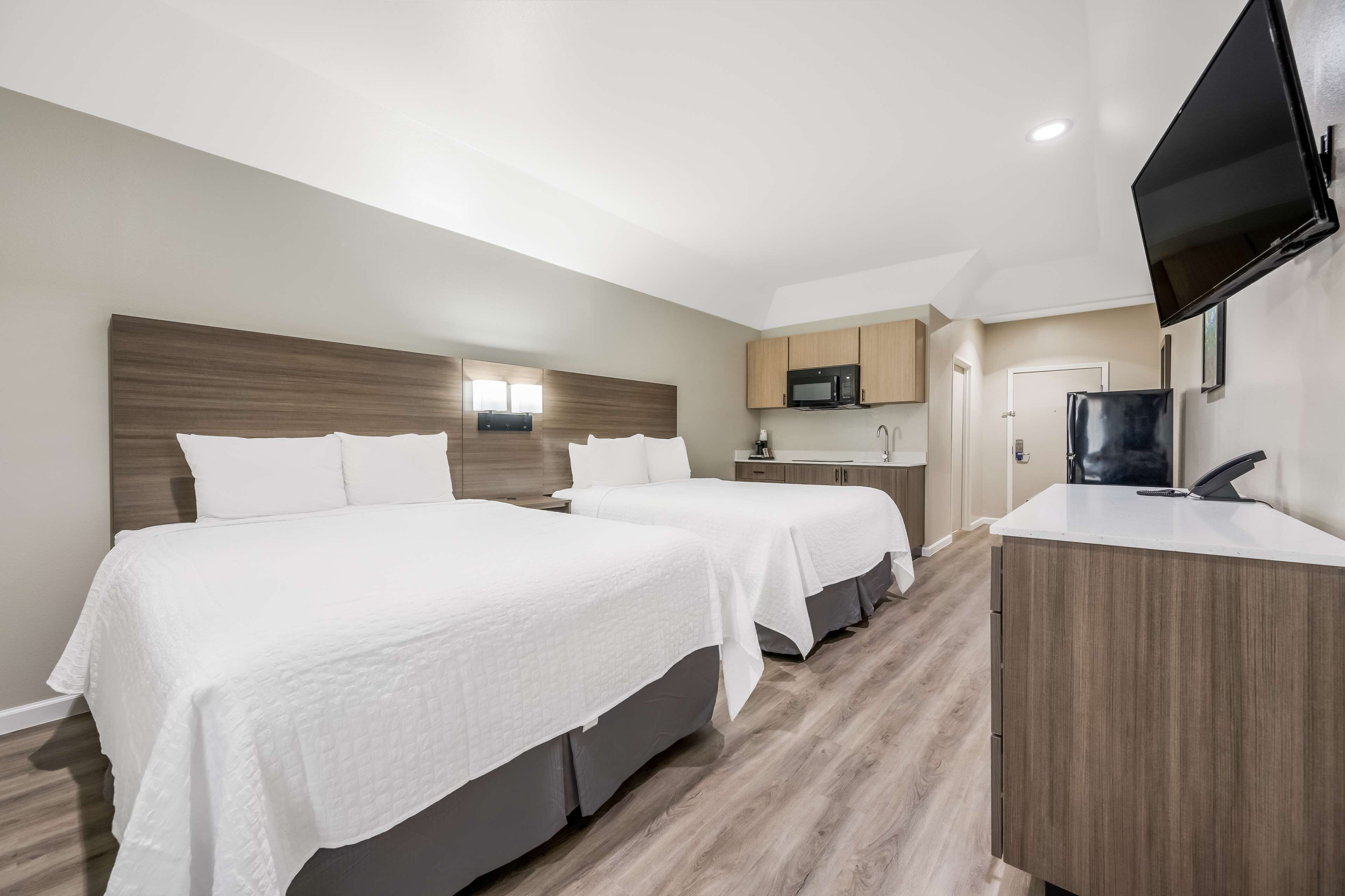 Une chambre d’hôtel avec deux lits, une kitchenette, un téléviseur à écran plat et une tête de lit en bois.