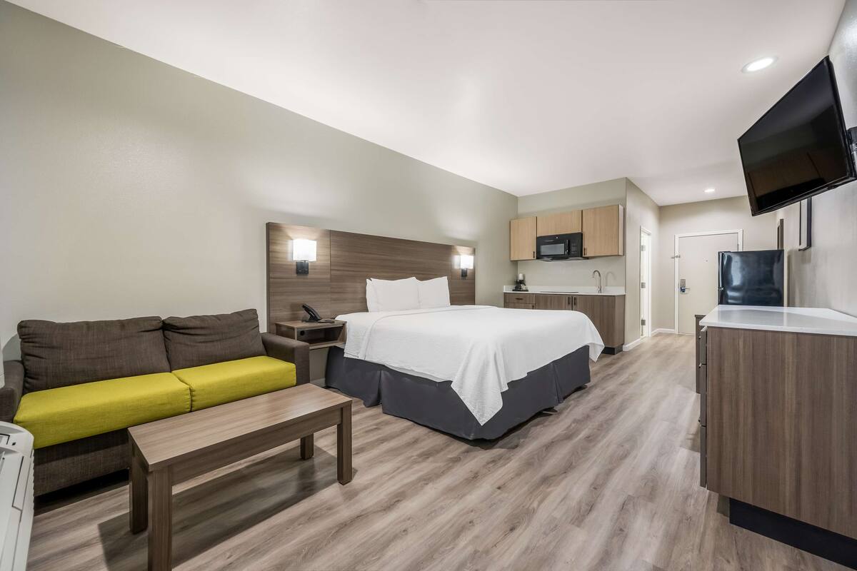 Een moderne hotelkamer met een bed, een bank, een klein tafeltje, een bureau, een televisie en een kitchenette.