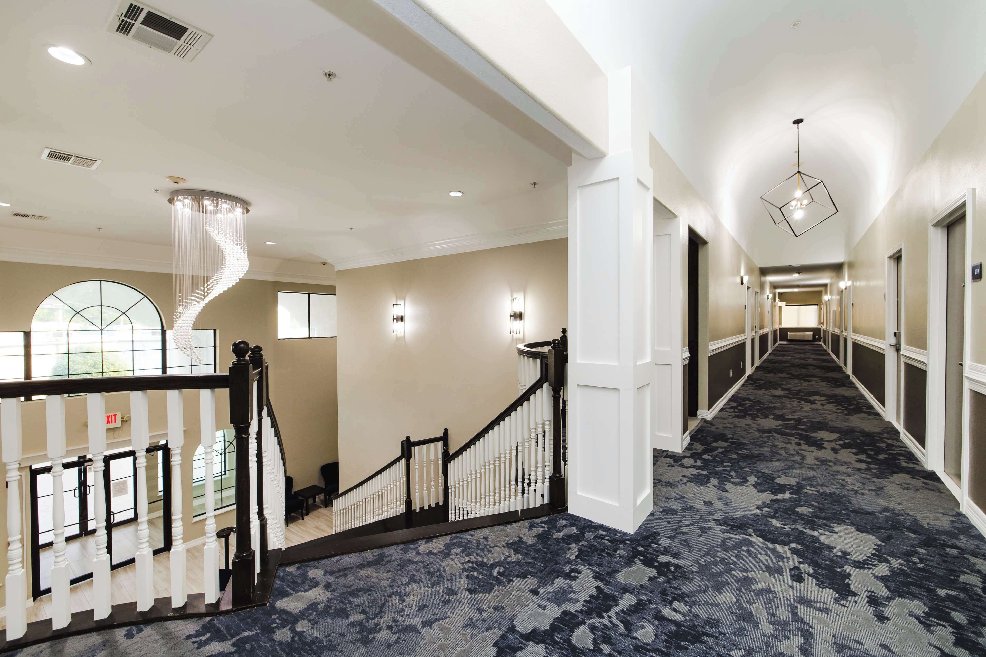 A hotel corridor with a grand staircase, a chandelier, and a patterned carpet.