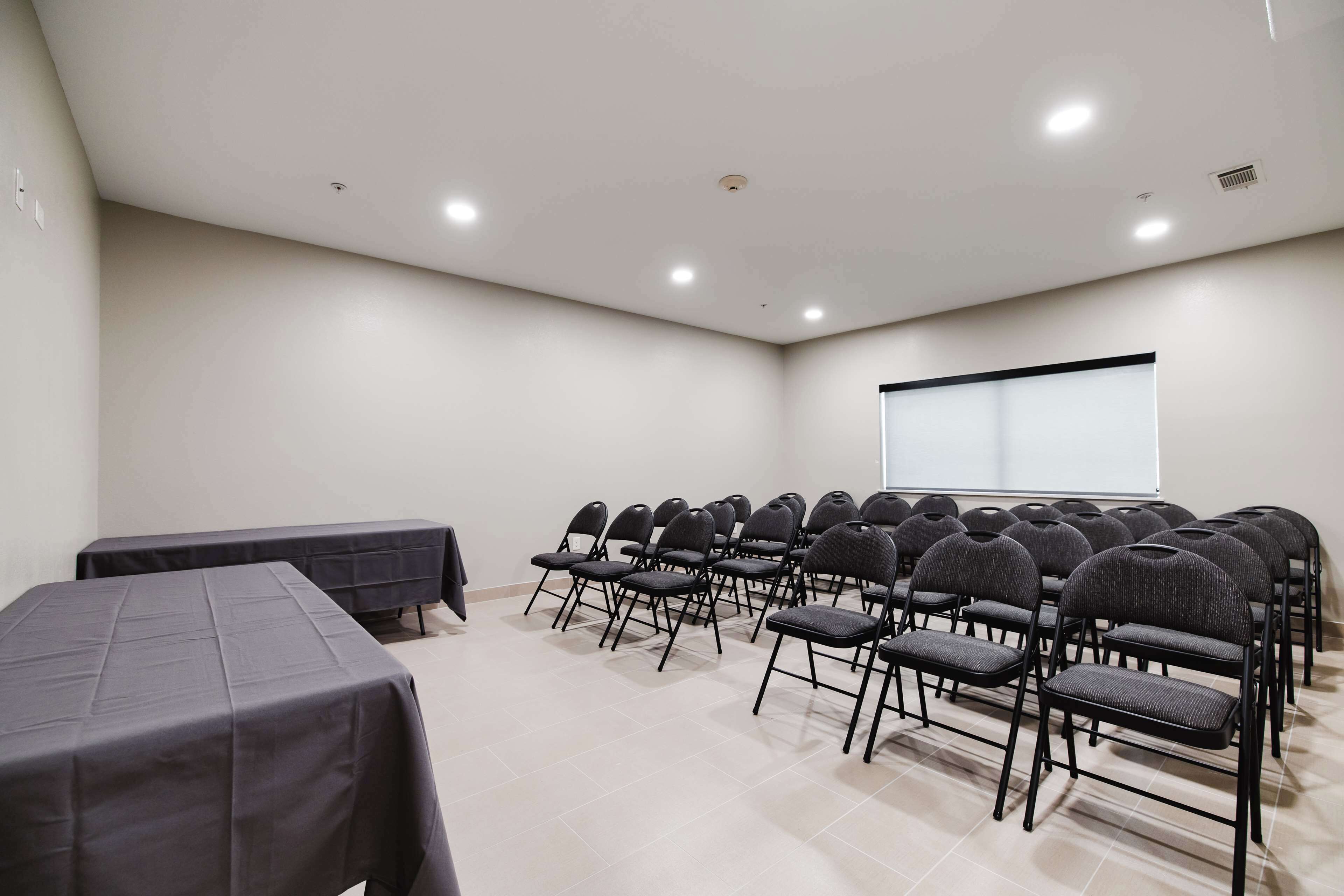 A conference room with rows of chairs, a projector screen, and tables with tablecloths.