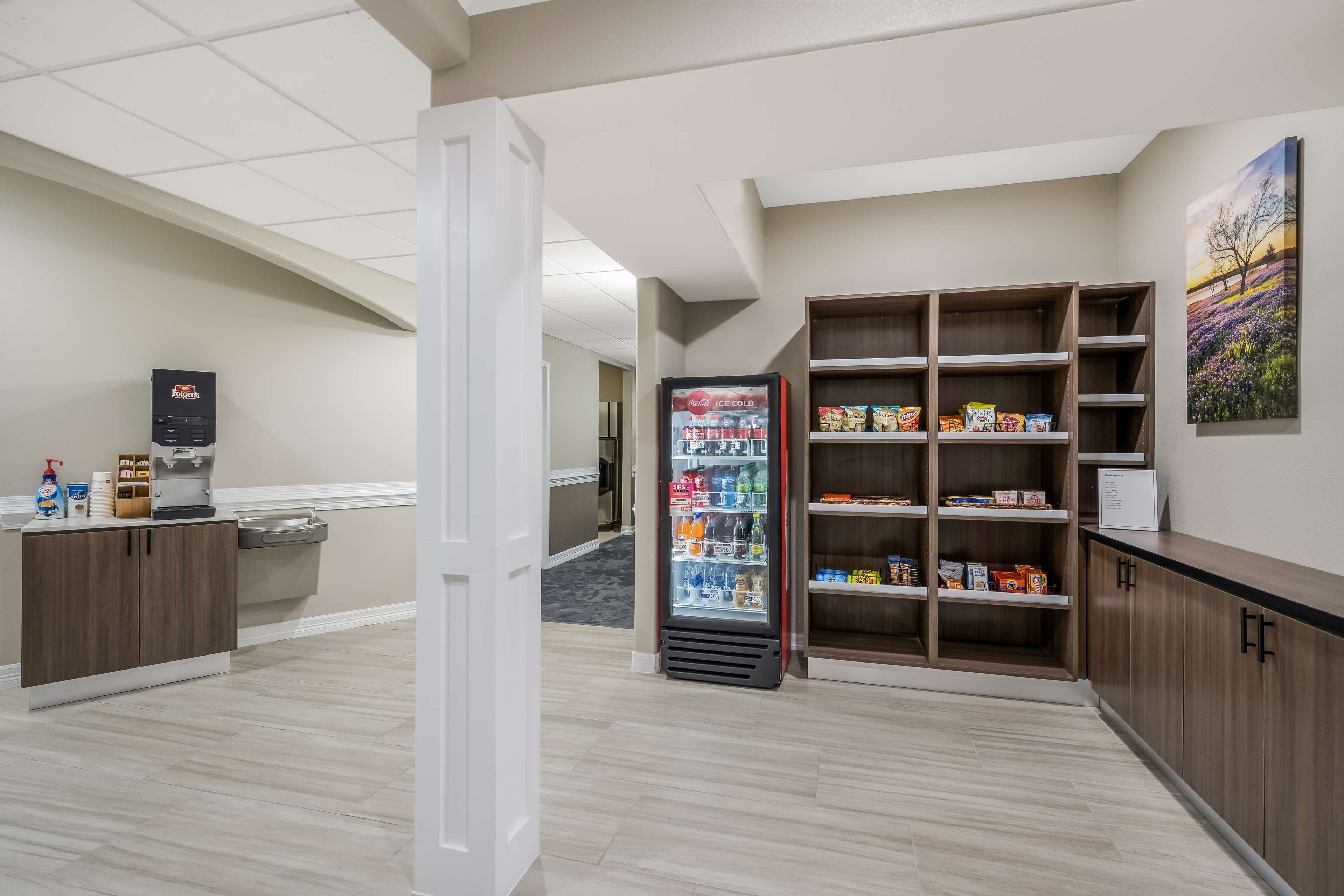 A hotel lobby with a vending machine, a refrigerator stocked with beverages, and a snack shelf.
