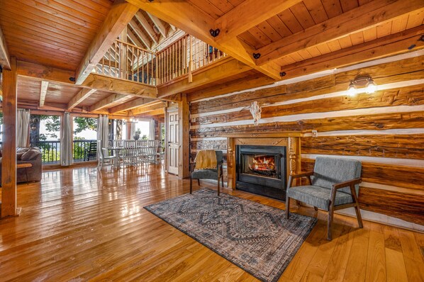 A spacious living room with a wooden floor, a fireplace, and a balcony with a railing.