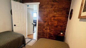 Une chambre avec deux lits, des murs en bois, une porte blanche et une petite table sur laquelle est posée une plante.