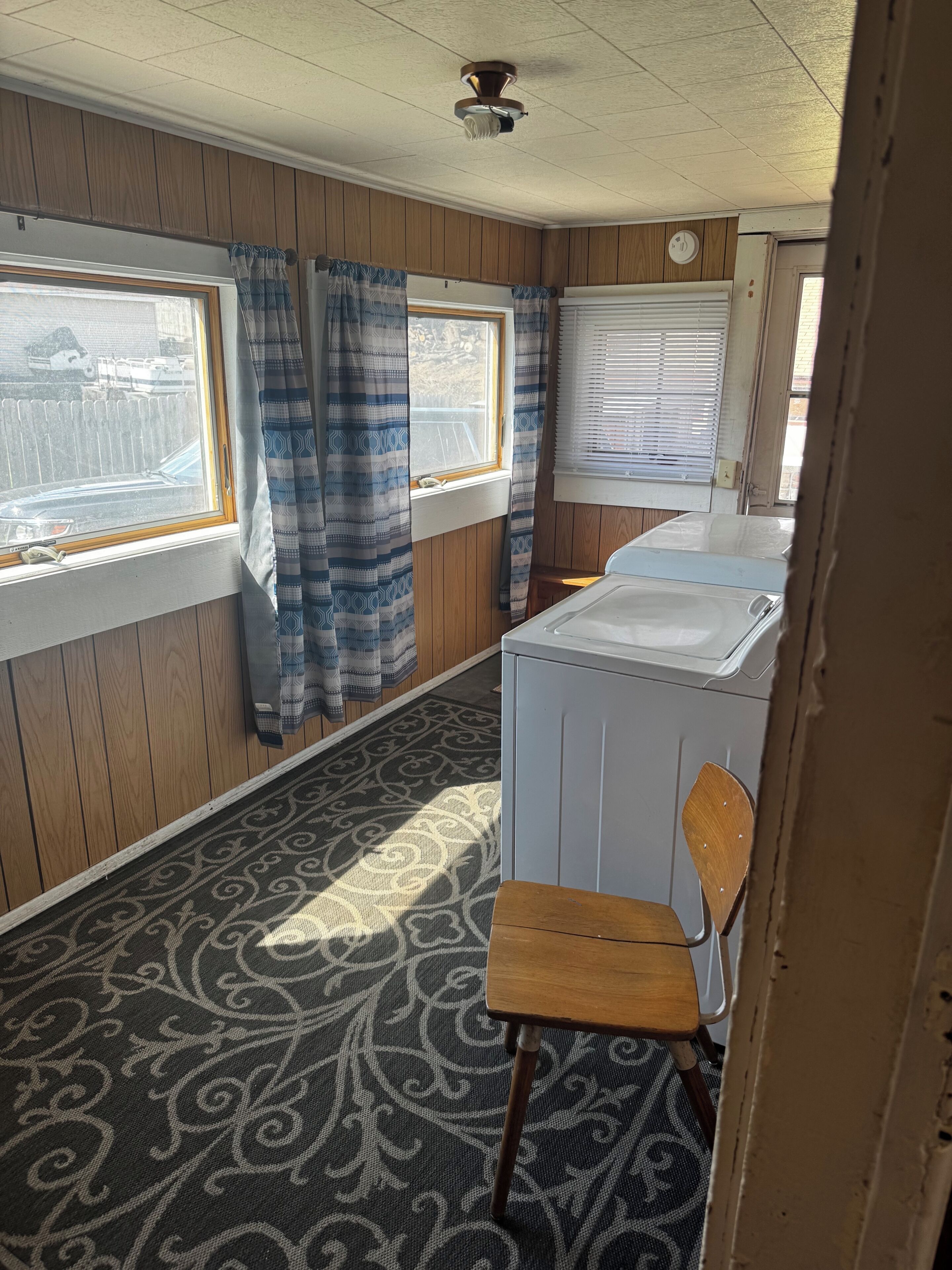 Una habitación compacta con ventana, lavadora, una silla y alfombra estampada.