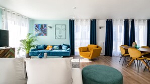 Ein modernes Wohnzimmer mit einer Couch, einem Sessel, einem Hocker und einem Essbereich mit Stühlen und einem Tisch.