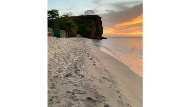 Ein Strand mit Fußabdrücken, die zum Wasser führen, einer Klippe und einem Sonnenuntergang.