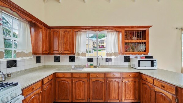Una cocina con armarios de madera, microondas y ventana con cortinas.