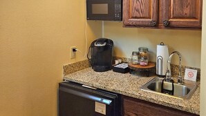 Une cuisine compacte avec des meubles en bois, un four à micro-ondes, une machine à café et un néon.