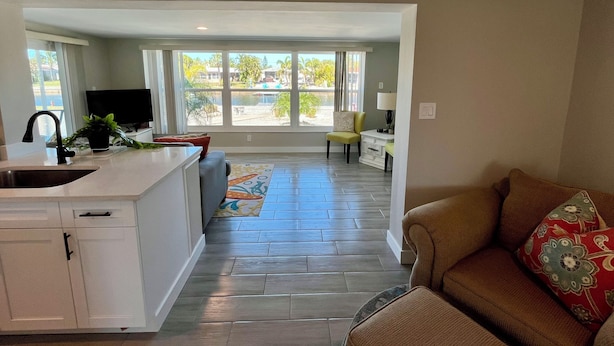 A spacious living area with a kitchen, a dining table, and a large window offering a view of the outdoors. - Beautifully remodeled in 2025. Gulf access. (New Port Richey)