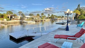 A waterfront patio with lounge chairs, a dock, and a calm water body. - Beautifully remodeled in 2025. Gulf access. (New Port Richey)