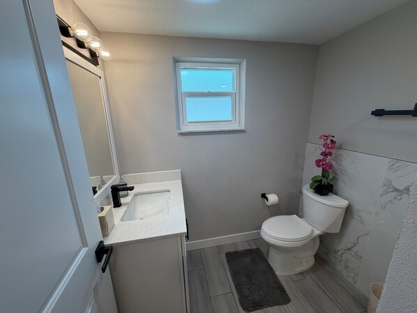 A compact bathroom with a white sink, toilet, and a small window. - Beautifully remodeled in 2025. Gulf access. (New Port Richey)