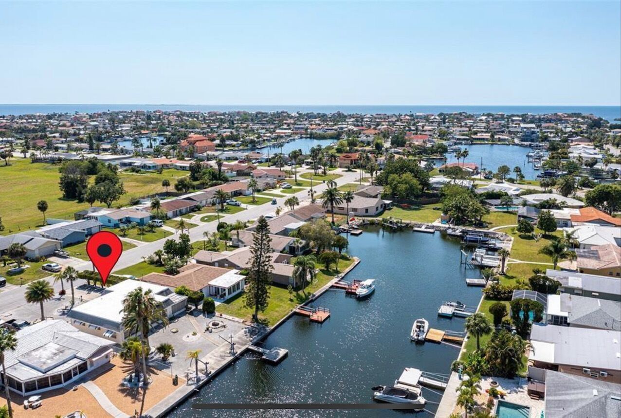 An aerial view of a coastal residential area with houses, a marina, and a large body of water.