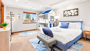 A bedroom with a bunk bed, a bedside table, a lamp, a painting, and a window with a view.