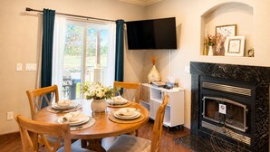 A dining area with a round table set for four, a fireplace, and a flat-screen TV mounted on the wall.