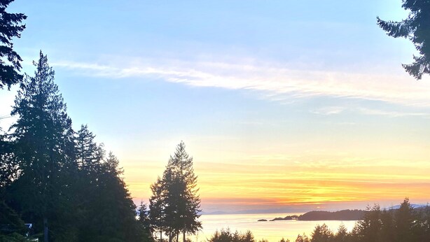 Un balcone con ringhiera in vetro che si affaccia su un panorama al tramonto, un pavimento in legno e un'area salotto esterna moderna.