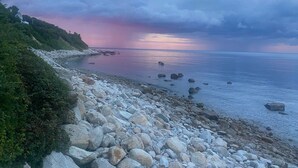 Kallioinen rantaviiva, josta avautuu näkymä merelle ja auringonlaskuun.