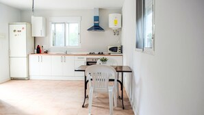 Een kleine keuken met witte kastjes, een magnetron, een fornuis en een raam.