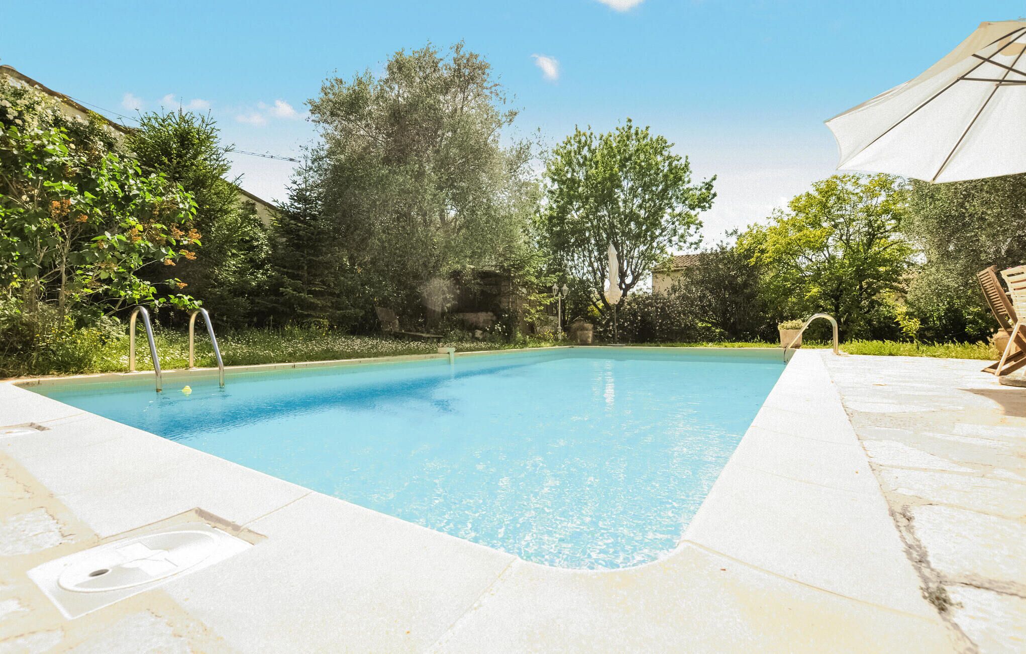 En swimmingpool med klart, blåt vand, omgivet af grønt og en stendækning.