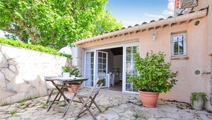 An outdoor patio with a stone table and chairs, potted plants, and a building entrance with glass doors. - Lovely home in Mouans-Sartoux with swimming pool (Mouans-Sartoux)