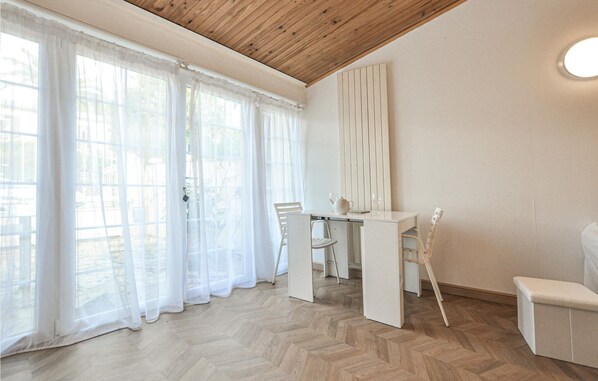 Une pièce avec un plafond en bois, une table blanche entourée de chaises et des rideaux légers aux fenêtres.