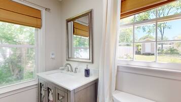 A bathroom with a white sink, a mirror, and a window with blinds.