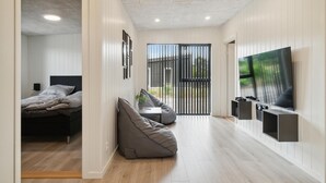 Una sala de estar moderna con una cama, sillón de peluche, televisor y puerta corredera que da a un balcón.