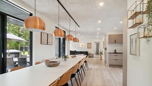 Una cocina moderna con armarios de madera, una mesa larga de comedor y luces colgantes.