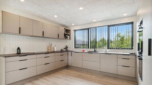 Una cocina moderna con suelo de madera clara, armarios blancos y un amplio ventanal con persianas verticales.