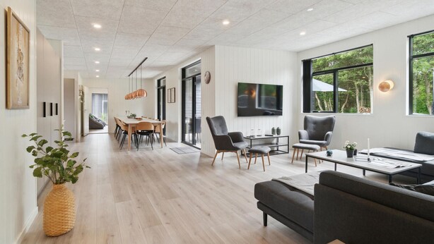 Un amplio salón con mesa de comedor, asientos cómodos, televisor de pantalla plana y ventanas grandes con vistas al exterior.
