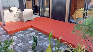 Eine moderne Terrassengestaltung mit rotem Deck, Korbmöbeln und einer Glastür zu einem Raum.