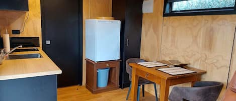 Een kleine kitchenette met een spoelbak, een koelkast en een vuilnisbak.
