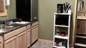 A kitchen with a black refrigerator, a coffee maker, and a 'Welcome' sign on the wall.